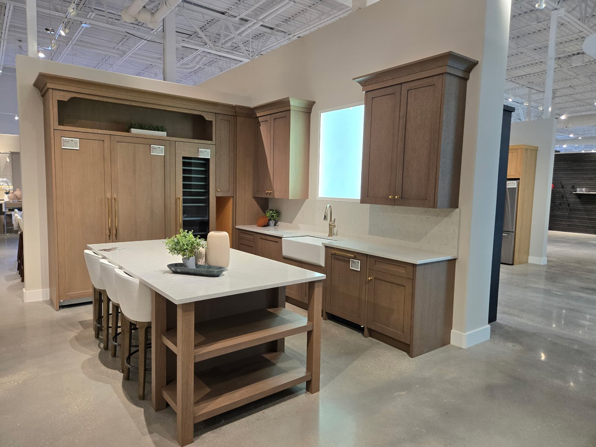 Modern kitchen display with light wood cabinets, white countertops, a farmhouse sink, and central island.
