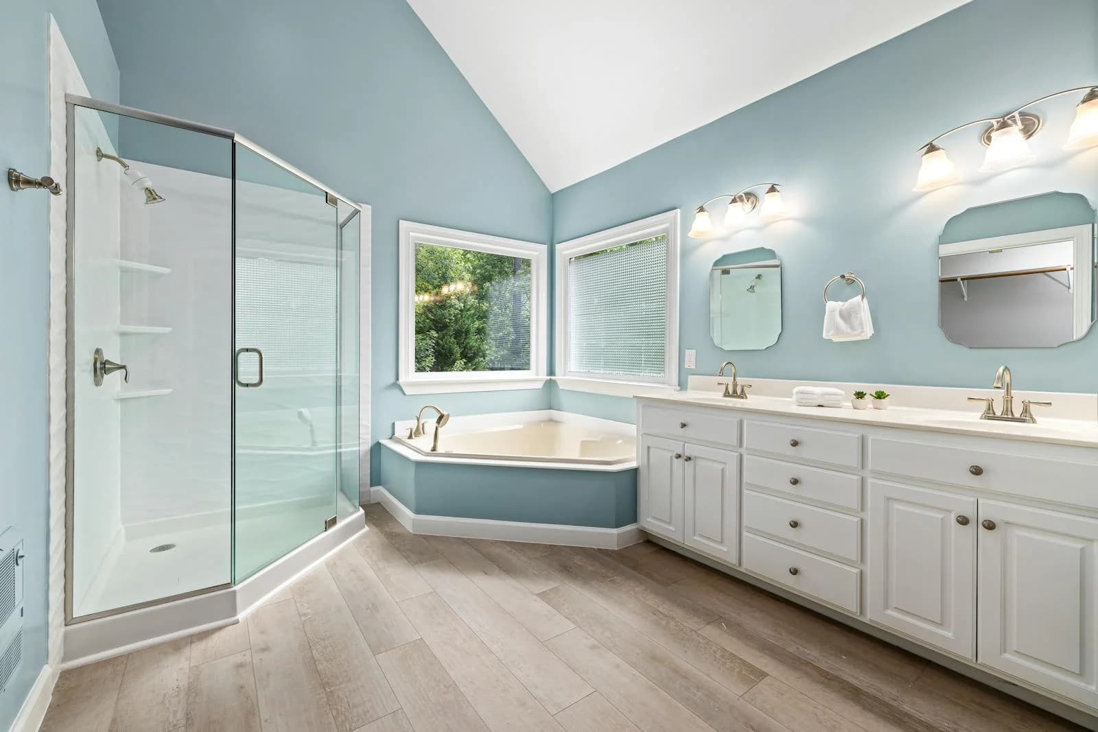 Light blue bathroom featuring a glass shower, corner bathtub, and a white double vanity.