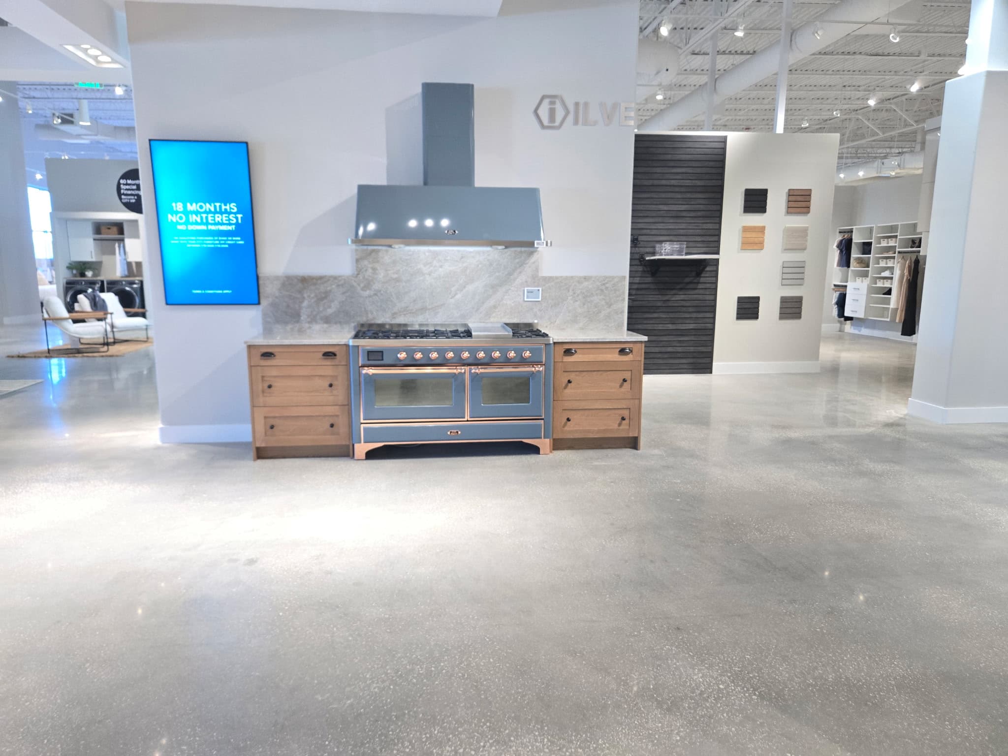Blue ILVE range and matching hood between wooden cabinets in a modern appliance showroom.