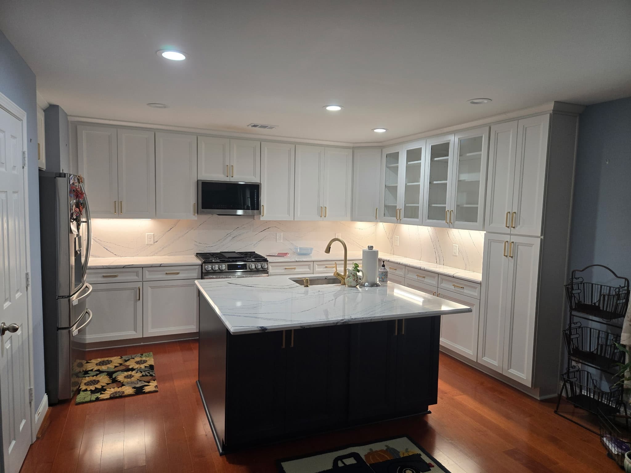 Modern kitchen with white cabinets, gold hardware, a dark island, and marble countertops.