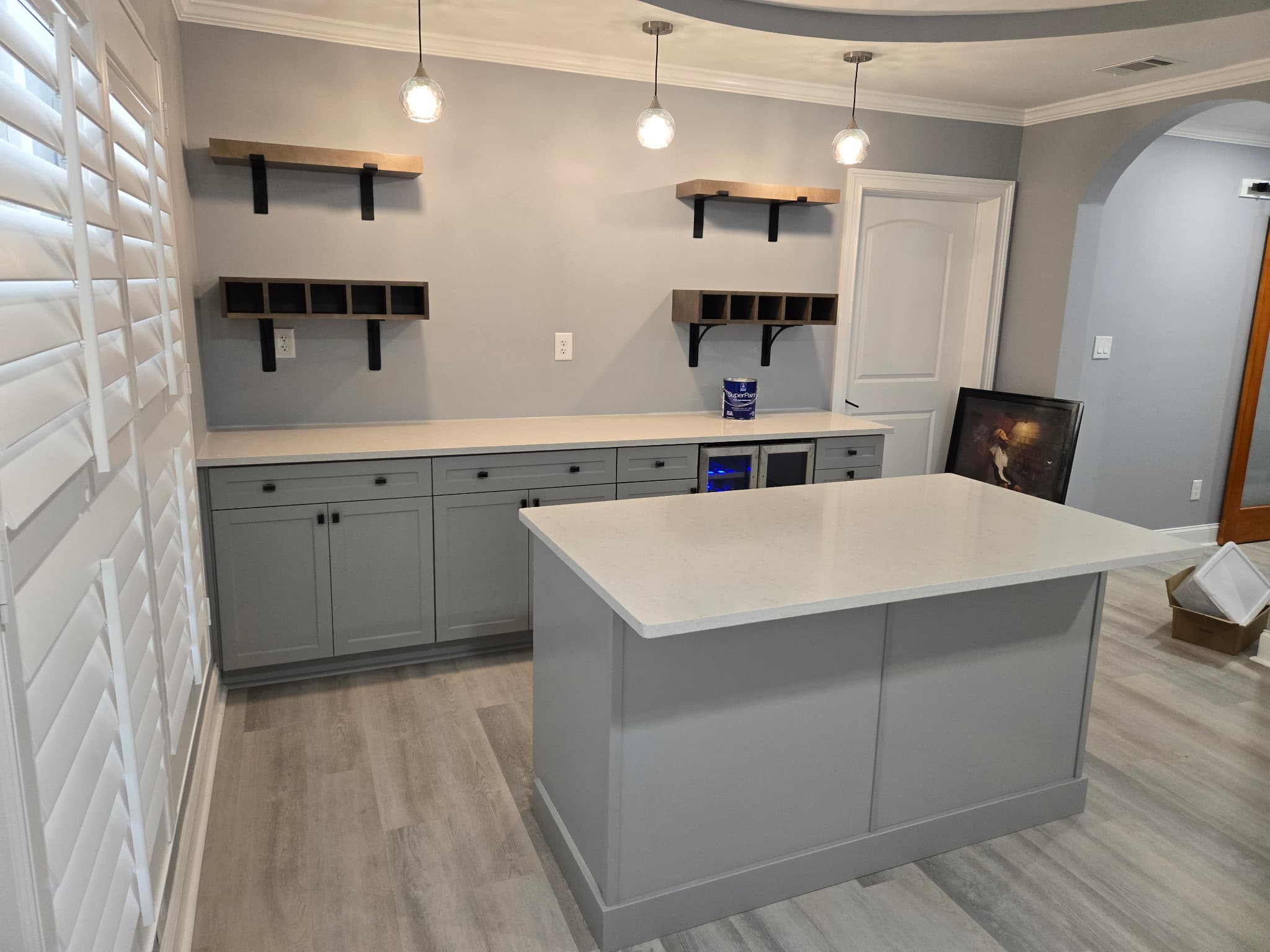 Modern gray kitchen featuring white countertops, a central island, floating shelves, and pendant lighting.